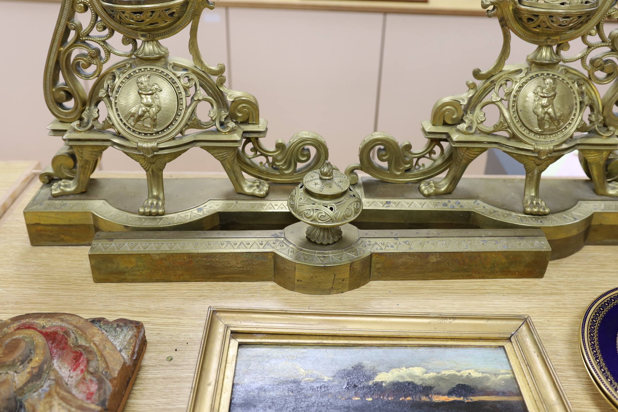 A pair of French bronze chenets, 19th century, with ornate decoration and cherub cartouche, adjustable curb, 64 cms high